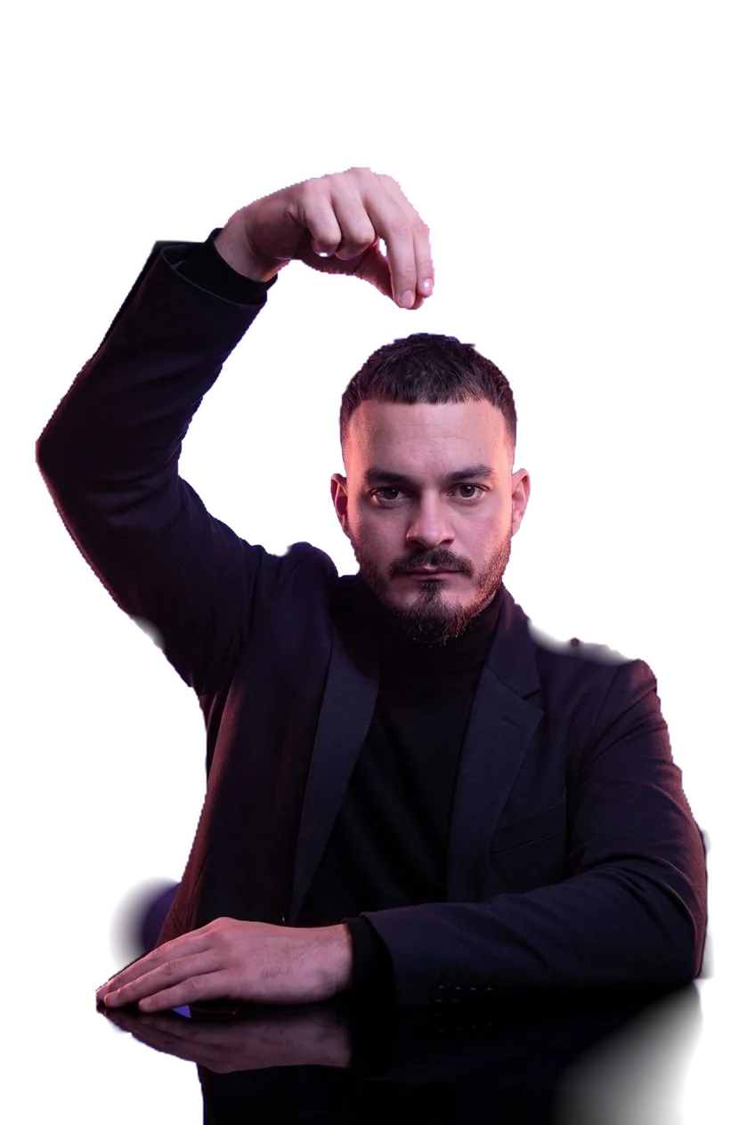 Serj, founder of GOAT BOLD, in a dark jacket, one hand raised above his head, the other resting on a table